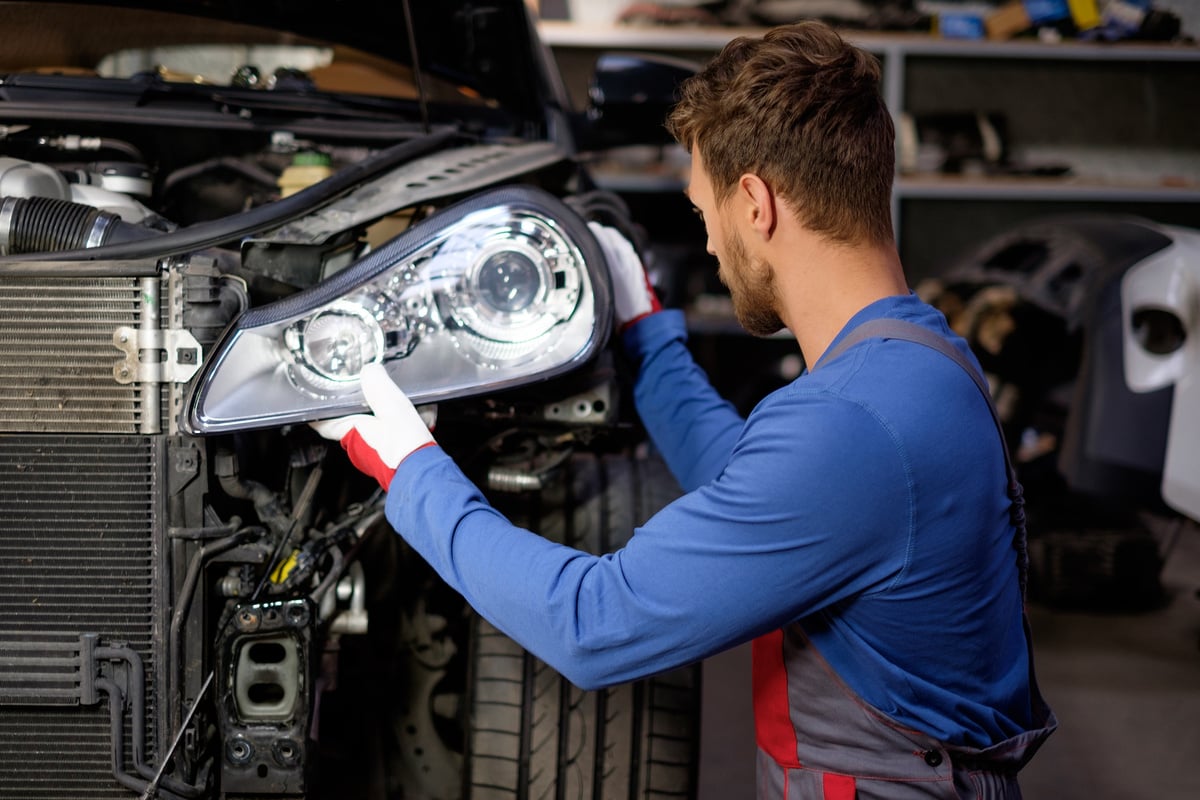 Mechanic with New Car Headlight in a Workshop